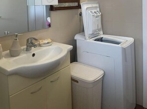 A bathroom with a sink, mirror, soap dispenser, and a white laundry machine. - Family house Kurtin by Brankica - Two bedroom apartment (Ugljan)
