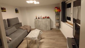 A living room with a grey sofa, a small table, a cabinet with decorations, and a television. - Vacation home in the heart of the Allgäu in Heimenkich (Heimenkirch)