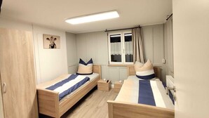 A room with two wooden beds, a window with curtains, a bedside table, and a wall-mounted picture. - Vacation home in the heart of the Allgäu in Heimenkich (Heimenkirch)