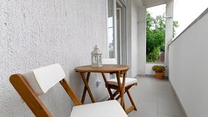 A balcony with a wooden chair and a small table, a potted plant, and a window with curtains. - Zadar Apartment Sweet Life - Studio Apartment with Balcony (Zadar)
