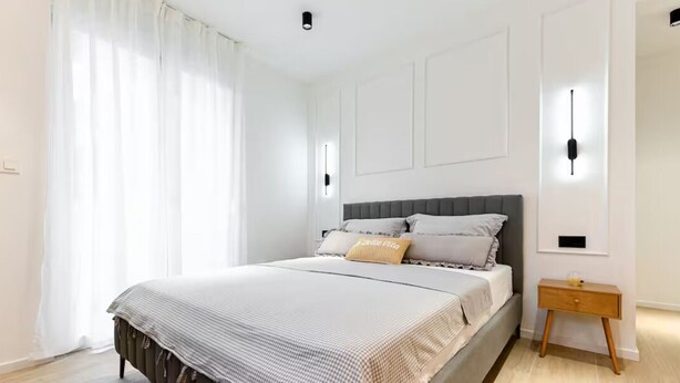 A bedroom with a large bed, white walls, a wooden floor, and a nightstand with a lamp. - Zadar Apartment Sweet Life - Studio Apartment with Balcony (Zadar)