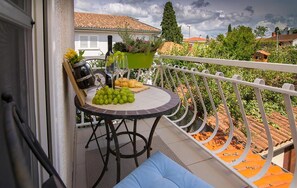 Ein Balkon mit Tisch, gedeckt für eine Mahlzeit, inklusive Trauben, Brot und einer Weinflasche.