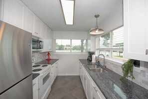 A modern kitchen with white cabinets, stainless steel appliances, a granite countertop, and a window providing natural light.