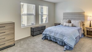 Ein Schlafzimmer mit Bett, Kommode, Nachttischen und einem Fenster mit Jalousien.