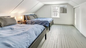 Ett litet, väl upplyst sovrum på vinden med två sängar, ett fönster och en spegel.