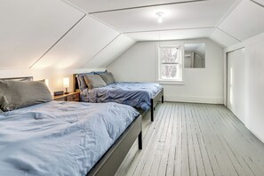 Une petite chambre mansardée, bien éclairée, avec deux lits, une fenêtre et un miroir.