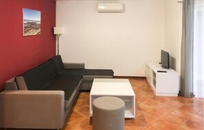 Un salon avec un canapé, une petite table, une lampe et un téléviseur posé sur un meuble.