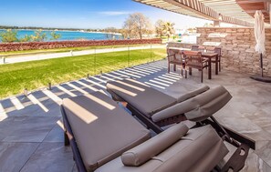 Eine Terrasse mit Liegestühlen, einem Tisch und Stühlen mit Blick auf ein Gewässer.