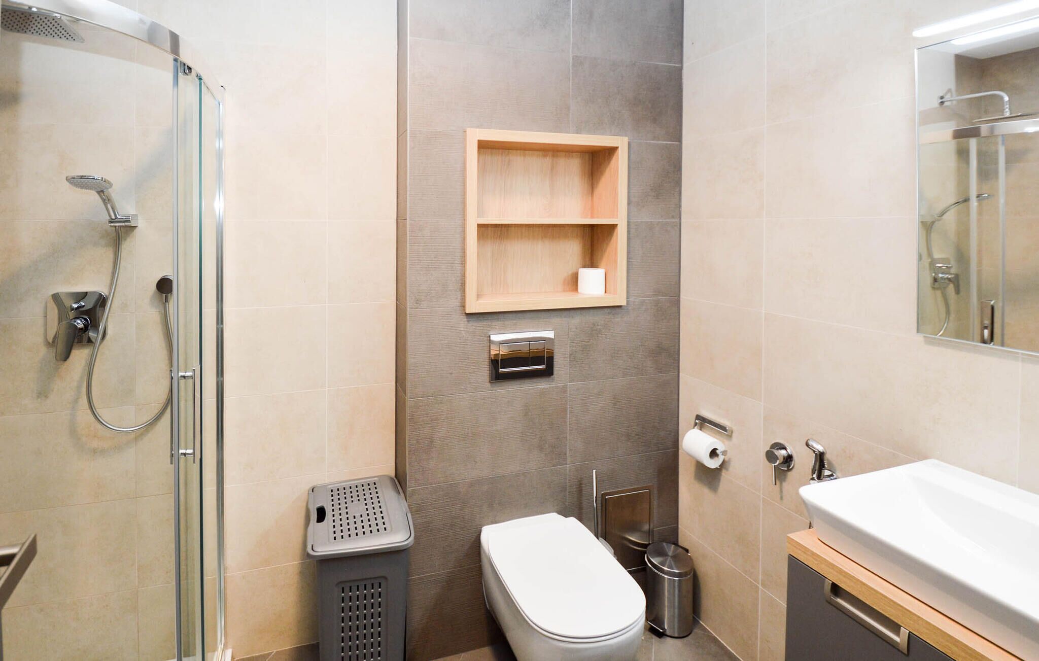 A modern bathroom with a glass shower enclosure, a toilet, a sink, and a wooden shelf with a toilet paper roll.
