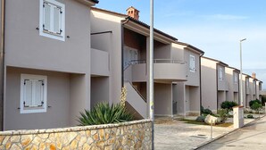 Une rangée d’immeubles résidentiels modernes à deux étages, dotés de balcons et de murs en pierre, sous un ciel dégagé.