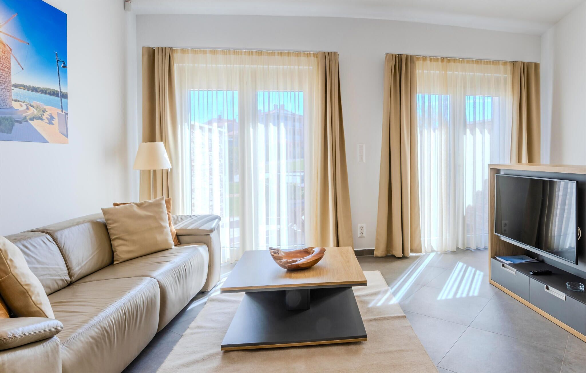 A modern living room with a sofa, a coffee table, a TV, and large windows with curtains.