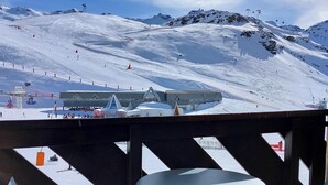 Une piste de ski enneigée avec un télésiège, un bâtiment doté d’un toit triangulaire, et une table et des chaises au premier plan.