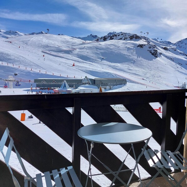 Ein verschneiter Skipisten mit Sessellift, ein Gebäude mit Satteldach und ein Tisch mit Stühlen im Vordergrund.