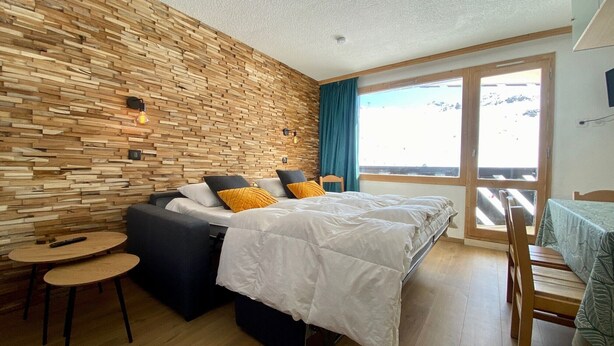 Une chambre moderne avec un mur en bois, un lit avec une literie blanche, une petite table et une vue sur l’extérieur.