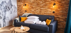 Ein moderner Raum mit einer Holzwand, einem dunklen Sofa, weißen Handtüchern und einem kleinen Holztisch.
