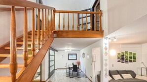 Eine Treppe führt zu einer oberen Etage, ein Essbereich mit Tisch und Stühlen sowie ein Wohnbereich mit einer Couch.