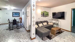 Ein Wohnzimmer mit einer Couch, einem Couchtisch und einem Fernseher. Es gibt einen Essbereich mit einem Tisch und Stühlen.