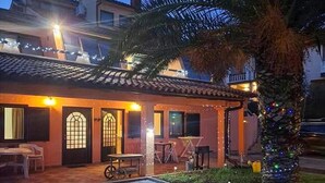 Ein Gebäude mit einem Ziegeldach, einer überdachten Terrasse mit Tischen und Stühlen sowie einer Palme.