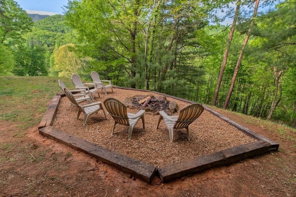 A circular seating area with four Adirondack chairs around a central fire pit, surrounded by a wooden border.