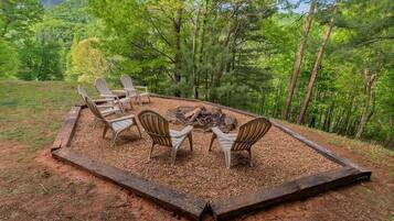 A circular seating area with four Adirondack chairs around a central fire pit, surrounded by a wooden border.