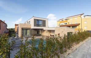Ein modernes, zweistöckiges Haus mit Swimmingpool, Steinaußenfassade und einer Terrasse mit Liegestühlen.