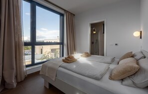 Ein modernes Hotelzimmer mit großem Fenster, Dusche und einem Bett mit Handtüchern und Kissen.