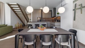 Une cuisine moderne dotée d’un îlot central, d’un coin repas avec une grande table et des chaises, et d’un escalier menant à un niveau supérieur.