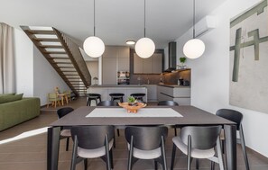 Eine moderne Küche mit einer zentralen Kochinsel, ein Essbereich mit großem Tisch und Stühlen sowie eine Treppe, die in einen oberen Bereich führt.
