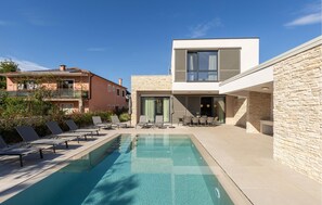 Ein moderner Poolbereich mit Liegestühlen und einem klaren Pool, umgeben von Steinmauern und einem zweistöckigen Gebäude mit großen Fenstern.