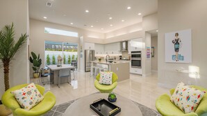 A spacious living area with a modern kitchen, green armchairs, and a dining table. - Brand New! Chic, Gated & Safe. Family & Pet Friendly, Sleeps 9 with Rec. Room… (Indio)