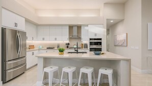 A modern kitchen with white cabinetry, stainless steel appliances, and a central island with stools. - Brand New! Chic, Gated & Safe. Family & Pet Friendly, Sleeps 9 with Rec. Room… (Indio)