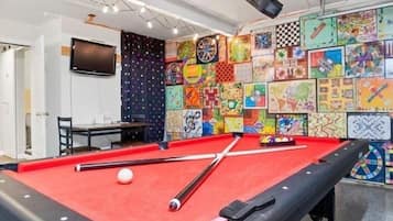 Ein Billardtisch mit roter Spielvliesdecke, umgeben von einer Wand mit verschiedenen farbenfrohen Kunstwerken.
