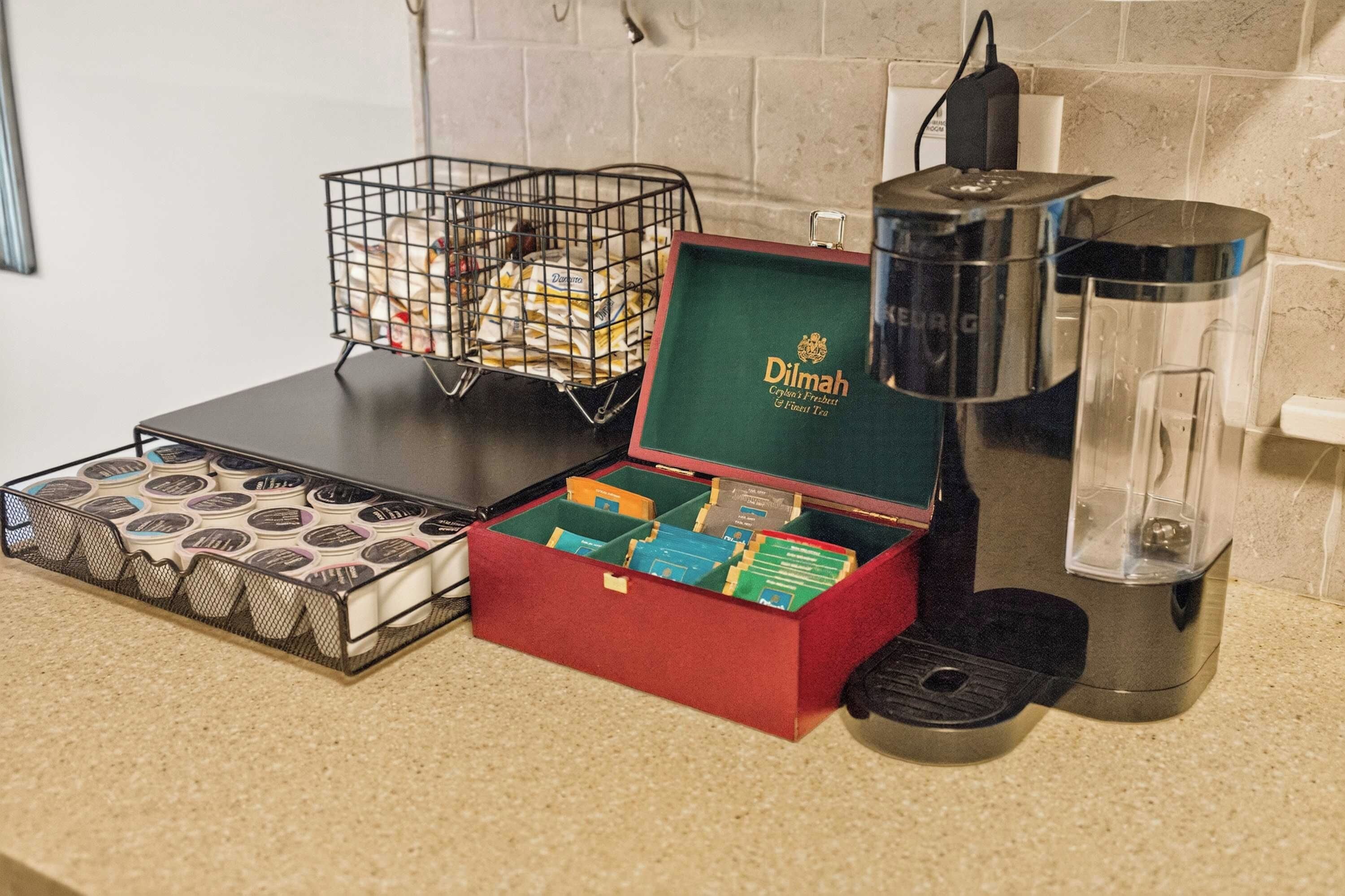 A kitchen area with a coffee maker, a basket of tea bags, and a box of tea.