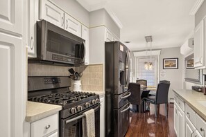 A modern kitchen with stainless steel appliances, white cabinetry, and a dining area with a table and chairs. - Canandaigua Lake Overlook (Canandaigua)
