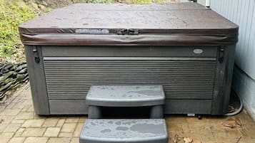 Uma banheira de hidromassagem com um banquinho em frente, colocada ao ar livre sobre um piso de tijolos.