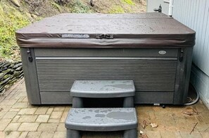 Ein Whirlpool mit einer kleinen Stufe davor, draußen auf einem Ziegelbelag.