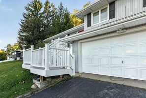 A residential house with a white garage door, a white porch with a railing, and a driveway. - Canandaigua Lake Overlook (Canandaigua)