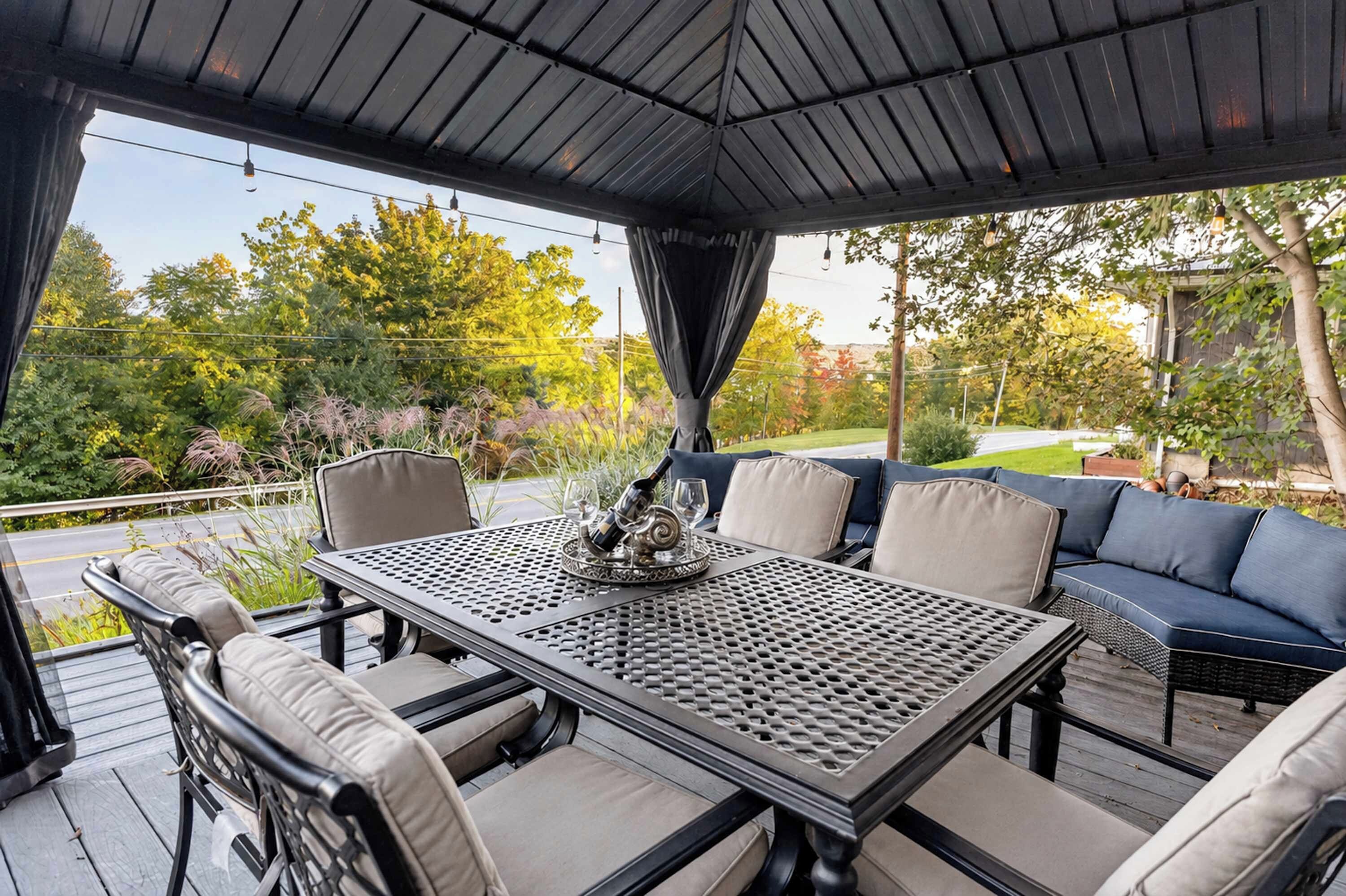 Une terrasse extérieure couverte, avec une table et des chaises, un canapé et une vue sur un jardin.