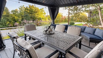 Un patio techado al aire libre con una mesa y sillas, un sofá y vistas a un jardín.