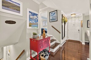 A hallway with a red console table, a staircase, and framed pictures on the walls. - Canandaigua Lake Overlook (Canandaigua)