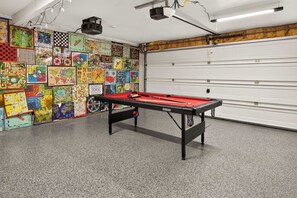 A room with a pool table, a variety of board games on the wall, and a garage door. - Canandaigua Lake Overlook (Canandaigua)