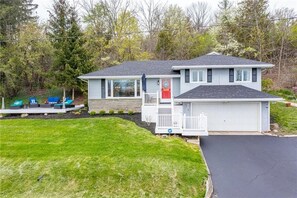A two-story house with a garage, a covered porch with seating, and a well-maintained lawn. - Canandaigua Lake Overlook (Canandaigua)