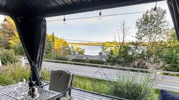 Un espace extérieur abrité, avec une table, des chaises et une vue sur une route et des arbres.