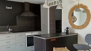 A modern kitchen with a central island, pendant lighting, and a small stool. - Cosy house + quiet garden with trees (La Brée-les-Bains)