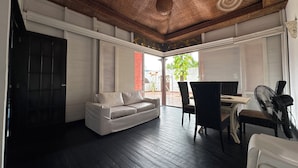 A room with a dark wooden floor, a white sofa, wicker chairs, a table, and a ceiling fan. - Auaecoco Hotel (Cartagena)