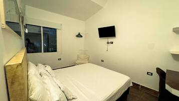 Un dormitorio con cama, ventana, televisor montado en la pared y una silla.