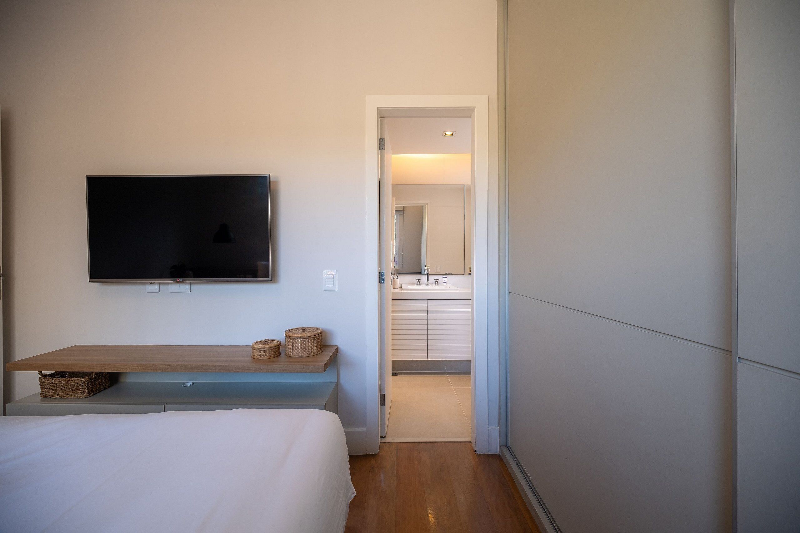 Ein Schlafzimmer mit einem Bett, einem an der Wand befestigten Fernseher, einer hölzernen Bank und einer Tür zu einem Badezimmer.