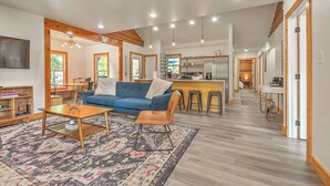 A spacious living area with a blue sofa, wooden coffee table, and patterned rug. A kitchen with a bar and stools is visible in the background. - Modern 4BD / 4.5BA Home Near ETSU, Mountain Home VA, JCMC, & Downtown JC (Johnson City)