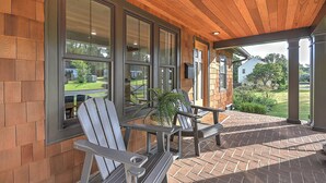 A covered patio with brick flooring, large windows, and Adirondack chairs. - Modern 4BD / 4.5BA Home Near ETSU, Mountain Home VA, JCMC, & Downtown JC (Johnson City)