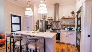 A modern kitchen with a central island, bar stools, stainless steel appliances, and pendant lighting.